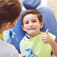 Child in dentist chair giving the thumbs up